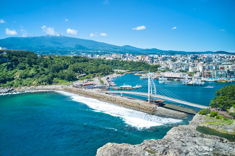 Seogwipo auf der  Jeju-Insel - Seyeon-Brücke, Stadt und Vulkan Hallasan - ©Hyeonsu - stock.adobe.com