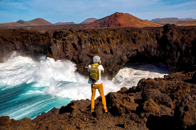Lanzarote - junge Frau fotografiert die felsige Küste von Los Hervideros mit Vulkane im Hintergrund - ©rh2010 - stock.adobe.com