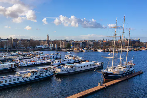 Amsterdam - Hafen mit Schiffen, traditionellen Segelbooten und Panoramablick auf die Stadt &ndash; &copy; Arkadii Shandarov - stock.adobe.com